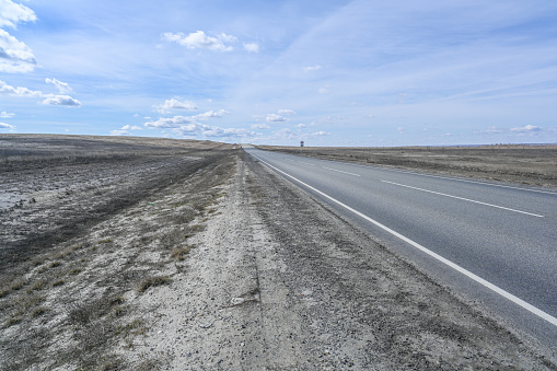 Highway road in the steppes, bushes, grass and cloudy sky. Spring landscape.