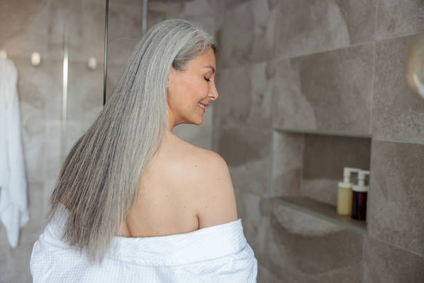 Beautiful lady is preparing to take bath Asian woman taking off her bathrobe to prepare to shower in the bathroom hair care women mature adult human skin stock pictures, royalty-free photos & images