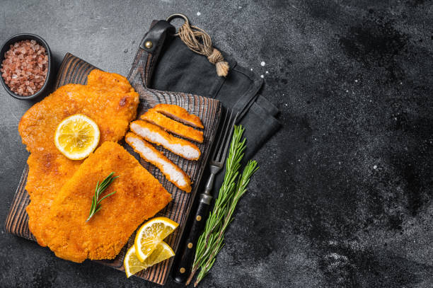 fried sliced weiner schnitzel on a wooden board with herbs. black background. top view. copy space - viennese schnitzel imagens e fotografias de stock