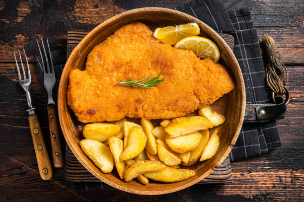 schnitzel frito austríaco com cunhas de batata em um prato de madeira. fundo de madeira. vista superior - produto de carne - fotografias e filmes do acervo