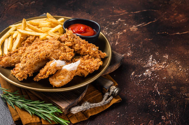 Fried Breaded chicken tender strips with french fries and tomato ketchup on a plate. Dark backgrund. Top view. Copy space Fried Breaded chicken tender strips with french fries and tomato ketchup on a plate. Dark backgrund. Top view. Copy space. chicken fried steak stock pictures, royalty-free photos & images