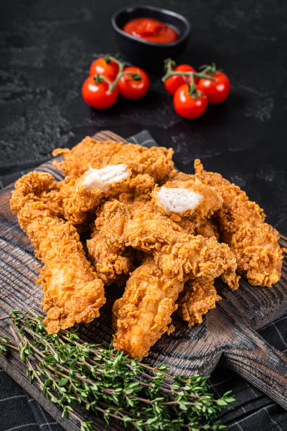 istock Dip fried Breaded chicken breast strips with tomato ketchup on a wooden board. Black backgrund. Top view 1368607097