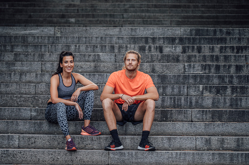 A sporty couple taking a break on the stairs during their daily workout.