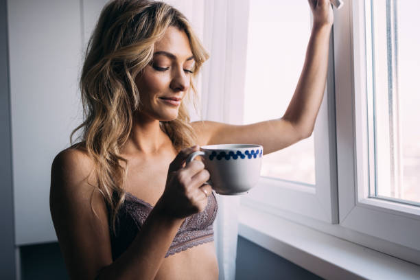 femme confiante buvant du café avant le travail, debout près de la fenêtre - the human body photos photos et images de collection