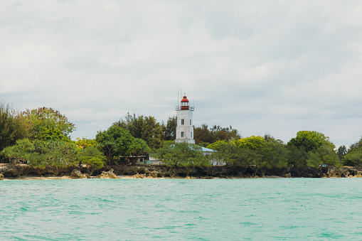 Sailing around the tropical island through the crystal blue sea and looking at the white lighthouse hidden in the forest in East Africa