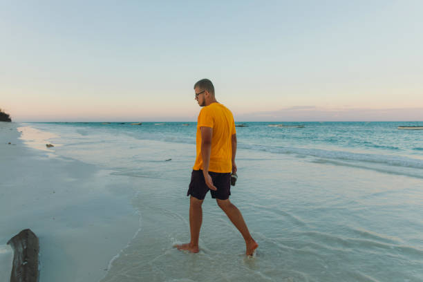 męski podróżnik kontemplujący zachód słońca na plaży na tropikalnej wyspie - men footprint beach sunset zdjęcia i obrazy z banku zdjęć