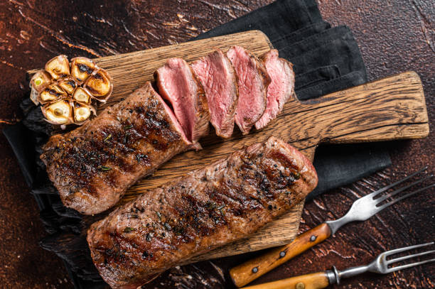 Grilled Lamb sirloin fillet meat on wooden board with herbs, mutton loin steak. Dark background. Top view Grilled Lamb sirloin fillet meat on wooden board with herbs, mutton loin steak. Dark background. Top view. Fillet Steak stock pictures, royalty-free photos & images