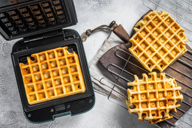 istock Cooking of fresh waffles in waffle maker. White background. Top view 1368610834