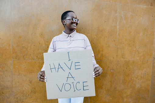 Young woman in front of the wall, standing and holding a sign 