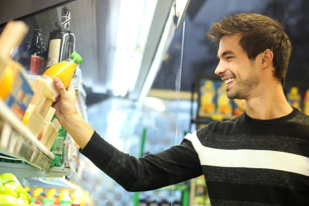 jeune homme achetant le jus d’orange - épicier photos et images de collection