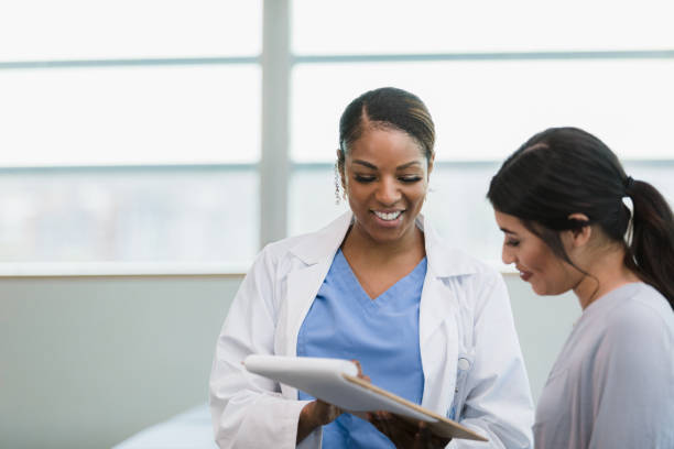 Smiling female doctor and happy female patient read medical chart A smiling mid adult female doctor and her happy young adult female patient read the test results on the medical chart together. woman talking to doctor stock pictures, royalty-free photos & images