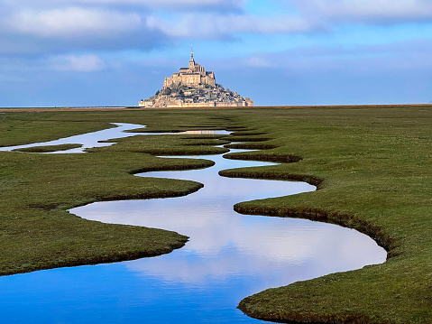 Salt marsh and Mont Saint-Michel landscape in normandy during sunny and cloudy day, UNESCO World Heritage Site in France, Europe.