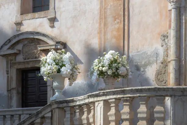 Romantic wedding bouquet in a baroque stone vase in front of the Chiesa di San Giuseppe in Taormina in Sicily, Italy