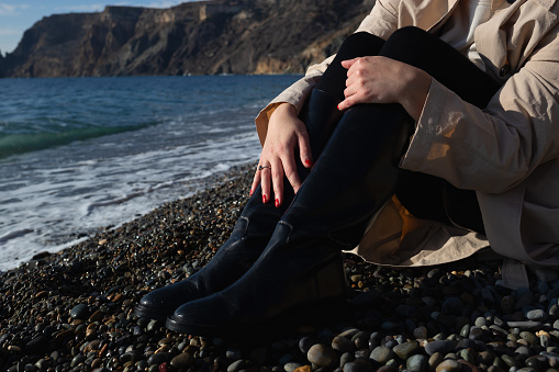 close-up shot. female hands hugging knees sitting on the seashore