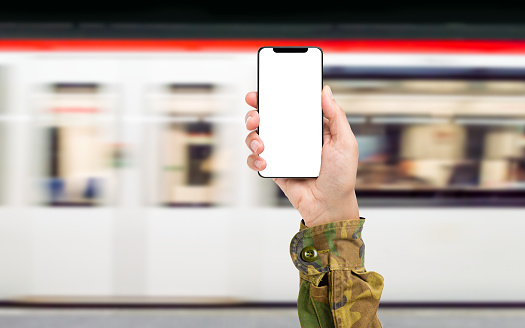 hand of a soldier with a phone with a subway or train in the background