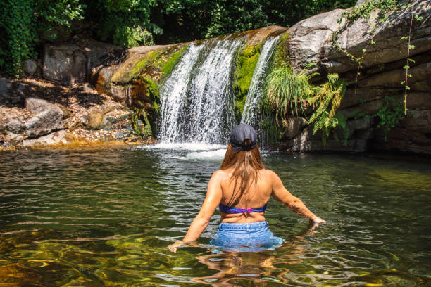 Rear view of a woman in a dress looking at waterfall during spring day in nature. Photographed in medium format.