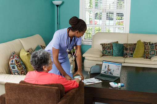 A home health nurse checking the vitals of a senior woman and using a medical device during an online consultation.