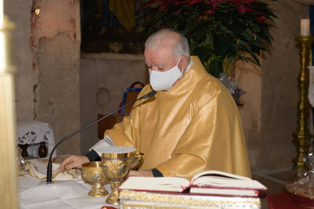 senior priest wearing a face mack preparing celebration of the sacrament of the eucharist - mask religious celebration horizontal easter imagens e fotografias de stock