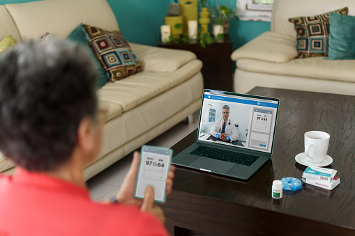 A latin senior woman at home using a medical device for a remote consultation with a doctor.