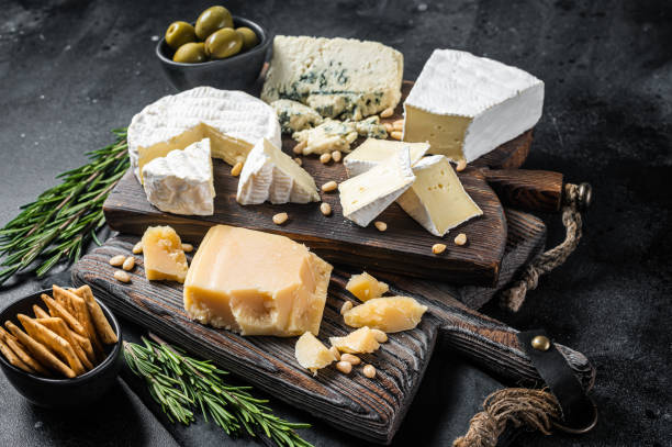 deliciosa tabla de quesos.  surtido de queso, camembert, brie, gorgonzola, parmesano, aceitunas, frutos secos y hierbas. fondo negro. vista superior - cheese softness freshness food fotografías e imágenes de stock