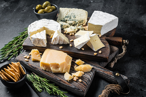 Delicious Cheese board.  Assortment of cheese, camembert, brie, Gorgonzola, parmesan, olives, nuts and herbs. Black background. Top view.