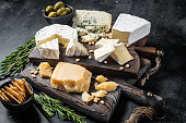 Delicious Cheese board.  Assortment of cheese, camembert, brie, Gorgonzola, parmesan, olives, nuts and herbs. Black background. Top view