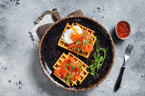 Belgian waffle with cream cheese, salmon slices, egg and red caviar. Gray background. Top view.