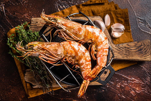 BBQ roasted Giant shrimps Langoustine on grill with herbs. Dark background. Top view.