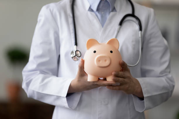 Crop close up female doctor physician holding pink piggy bank Crop close up female doctor physician nurse wearing white uniform with stethoscope holding pink piggy bank, medical insurance concept, healthcare and medicine, hospital budget, clinic fees operating budget stock pictures, royalty-free photos & images