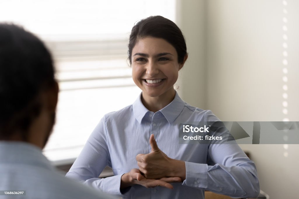 Smiling young Indian woman who is deaf using sign language Smiling young Indian woman who is deaf using sign language, communicating with friend or doctor physician, happy attractive female having fun and enjoying pleasant conversation, hard of hearing Translation Stock Photo