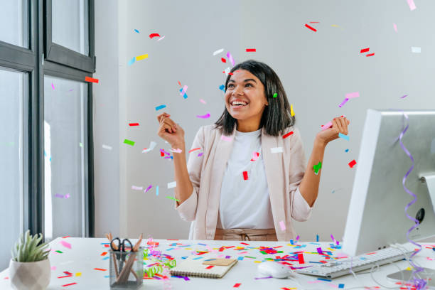 joven empresaria divirtiéndose atrapando confeti - aniversario fotografías e imágenes de stock