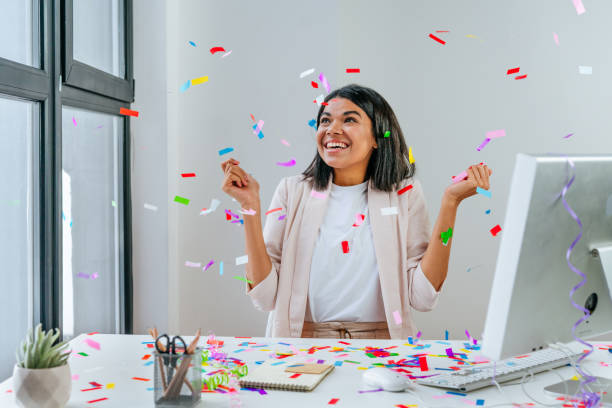 Young business woman having fun time catching confetti Young business woman having fun time catching confetti sitting at the desk in the office. Party time on the work place. Selective focus. celebration event stock pictures, royalty-free photos & images