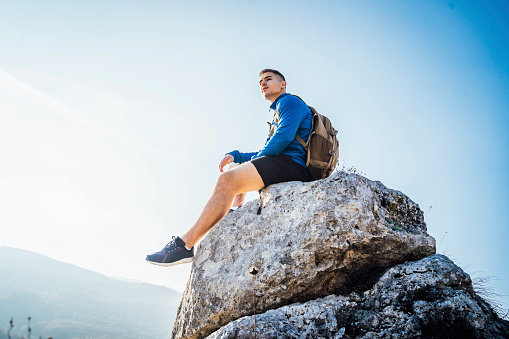 Young caucasian man sitting at the top of mountain and looking at view