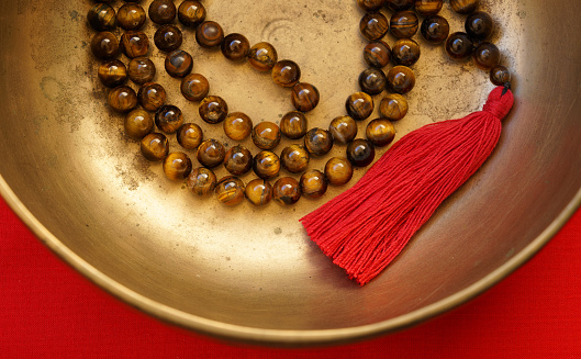 Tiger's Eye beaded mala meditation necklace with red tassel inside an antique Tibetan singing bowl.