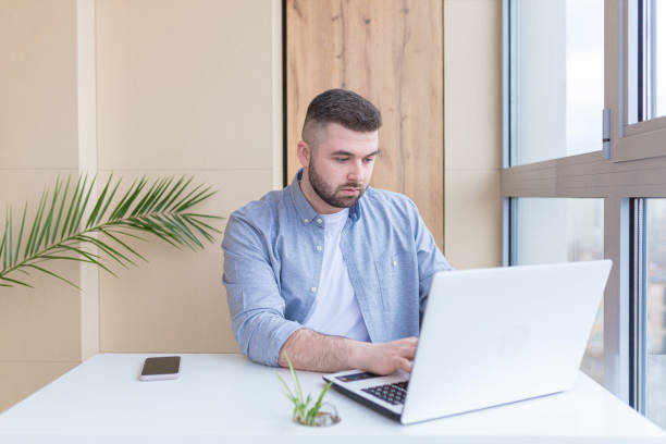 istock young man working, studying, on laptop and talking on the phone, at home, sitting at a table by the window 1368643011