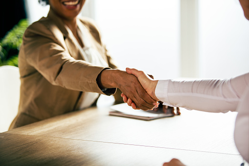 Close up shot of two diverse, unrecognizable businesswomen sitting on the opposite sides of the conference table and shaking hands after a successful meeting.