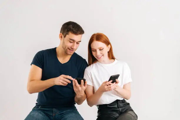 Photo of Studio shot of young handsome man showing new mobile software app to smiling girlfriend on white isolated background.