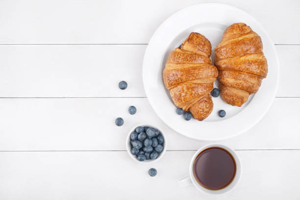 черничные круассаны и черный чай на белом деревянном фоне - croissant morning white breakfast стоковые фото и изображения