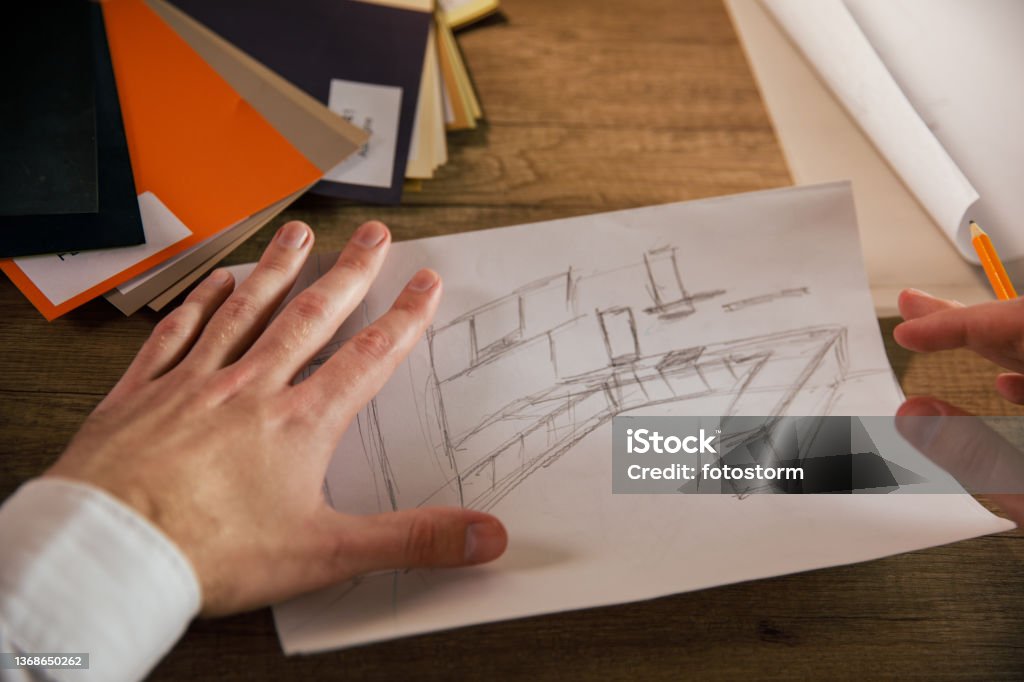Architect working on a sketch of interior design for a project Personal perspective of male architect sitting at his desk and working on a sketch of interior design for a project. Drawing - Activity Stock Photo Architect working on a sketch of interior design for a project Personal perspective of male architect sitting at his desk and working on a sketch of interior design for a project. Drawing - Activity Stock Photo