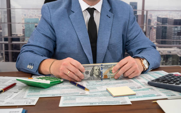 istock A handsome man in a black stylish suit at a spacious table counts dollars and fills out forms. 1368650304