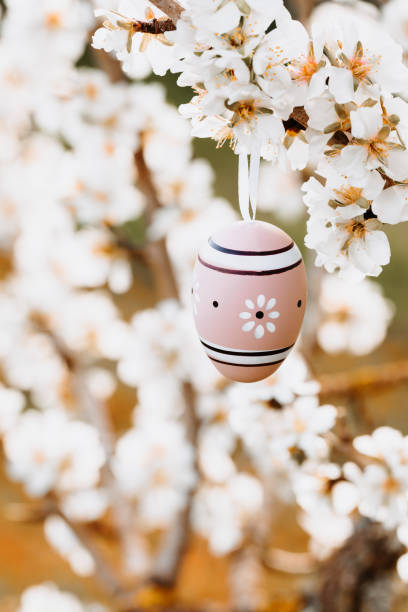 istock Boho easter egg with a painted flower in beige and brown tones hanging in between almond blossoms on an almond tree 1368650334