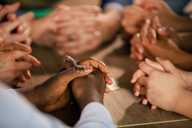 istock Group of diverse people sitting around a table, hands clasped 1368650366