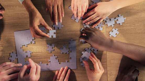 Directly above shot of group of unrecognizable friends hanging out and having fun by assembling a jigsaw puzzle together.