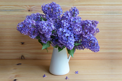 Beautiful lilac flowers in vase on wooden background