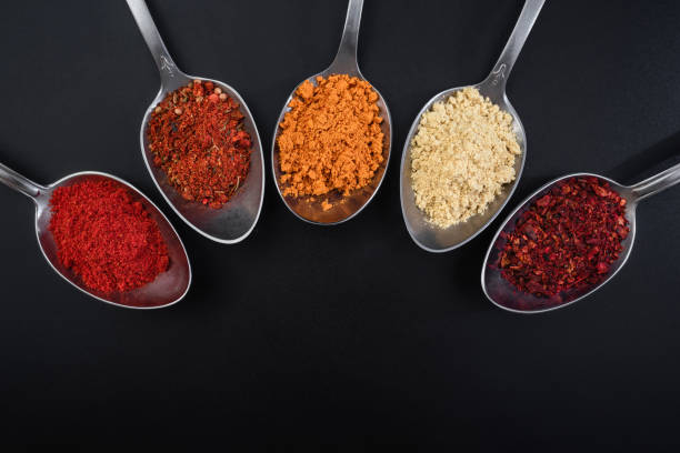 Colored spices in spoons on a black background, top view. Indian spices