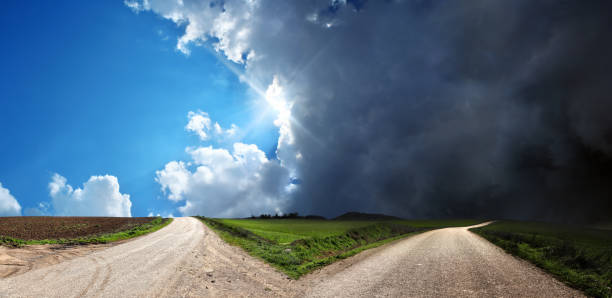 pusta rozwidlona droga nad konceptualnym dramatycznym niebem - sunbeam cloud panoramic sky zdjęcia i obrazy z banku zdjęć