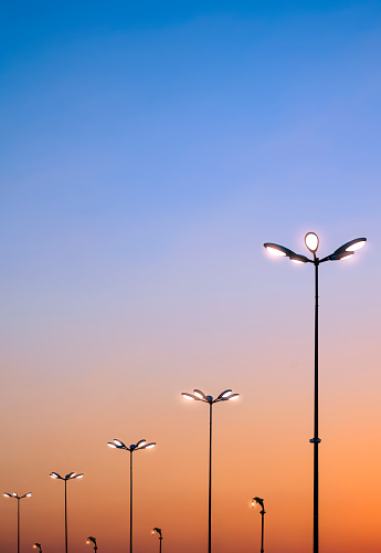 Silhouette row of modern and retro street lamp posts against sunset sky background in vertical frame