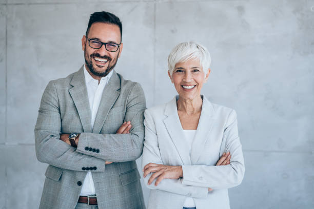 Business people in the office. Shot of two confident business persons standing side by side with folded arms in the office. Portrait of successful businessman and businesswoman posing together in their office. side by side stock pictures, royalty-free photos & images