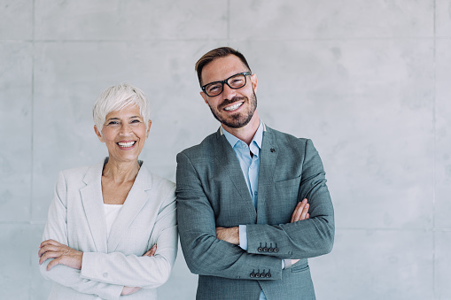 Shot of two confident business persons standing side by side with folded arms in the office. Portrait of successful businessman and businesswoman posing together in their office.