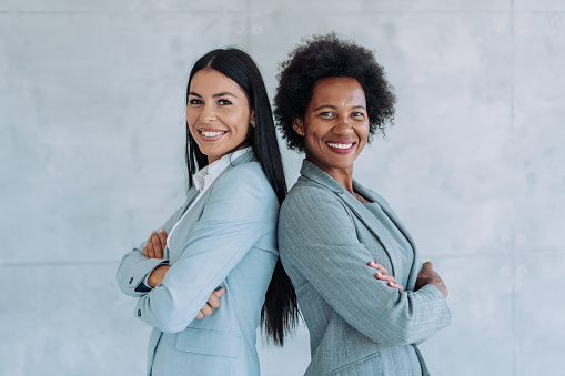 Shot of two confident businesswomen standing back to back and keeping arms crossed while looking at camera.